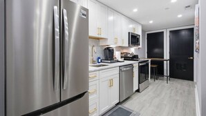 Una cocina moderna con electrodomésticos de acero inoxidable, armarios blancos y una puerta negra.