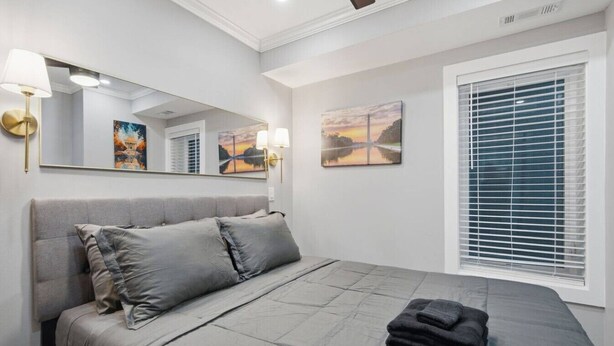 Un dormitorio con cama, ventana con persianas, espejo en la pared y una obra de arte.