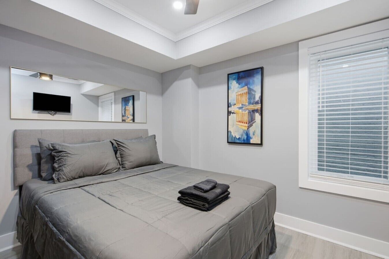 Une chambre à coucher avec un lit, un téléviseur à écran plat, un tableau et une fenêtre avec des stores.