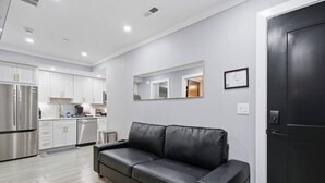 Cocina moderna con gabinetes blancos y electrodomésticos de acero inoxidable, sofá de cuero negro y una puerta oscura.