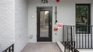Entrada de un edificio con una puerta negra, un detector de incendios y una ventana con persianas.