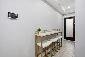 Un interior moderno con una pared blanca, una pequeña planta en maceta, un taburete blanco y una puerta negra.