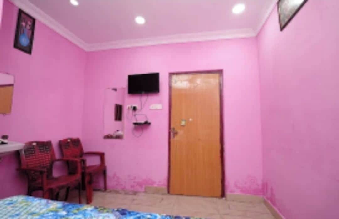 A pink-walled room with a bed, a television, and a wooden door.