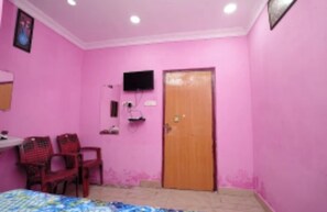 A pink-walled room with a bed, a television, and a wooden door. - Sri Balaji Hotel  (Vijayawada)