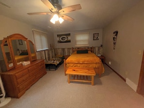 A bedroom with a bed, a dresser, a bench, a ceiling fan, and a window with blinds. - Spacious 5 bedroom kid friendly home. Private backyard. 1.5 miles from Lambeau (Green Bay)