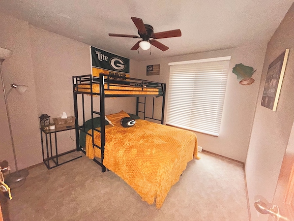 A bunk bed with a ceiling fan, a window with blinds, and a door with a doorknob.