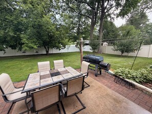An outdoor patio with a table and chairs, a grill, and a garden area.