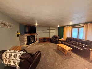 A living room with a fireplace, leather sofas, a television, and a sign that reads 'WISCONSIN'. - Spacious 5 bedroom kid friendly home. Private backyard. 1.5 miles from Lambeau (Green Bay)