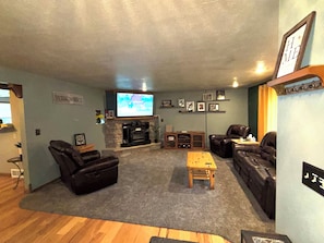 A living room with a fireplace, leather sofas, a coffee table, and a television mounted on the wall. - Spacious 5 bedroom kid friendly home. Private backyard. 1.5 miles from Lambeau (Green Bay)