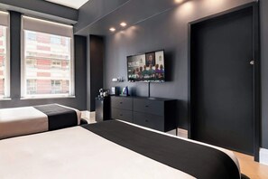 A modern hotel room with a large bed, a flat-screen TV mounted on the wall, a small desk with a coffee machine, and a view of the city through large windows. - Two-Bedroom Suite by Madison Square Park (New York)