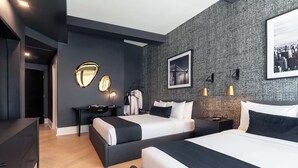 Moderni hotellihuone, jossa on kaksi sänkyä, työpöytä, tuoli, vaatekaappi ja peili.