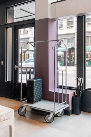 A luggage cart with a suitcase and a black umbrella stand with umbrellas. - Two-Bedroom Suite by Madison Square Park (New York)
