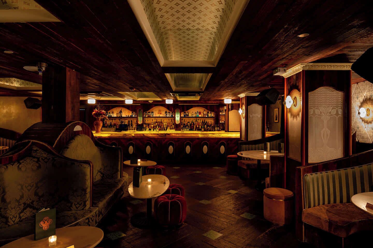 Zona de bar con suelo de madera, taburetes y barra.