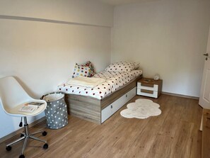 Une chambre à coucher avec un lit, une chaise, une petite table et une poubelle.