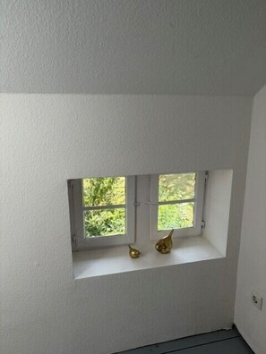 Ein kleines Fenster mit zwei Scheiben, einer weißen Fensterbank und zwei kleinen, goldenen Dekorationen auf der Fensterbank.