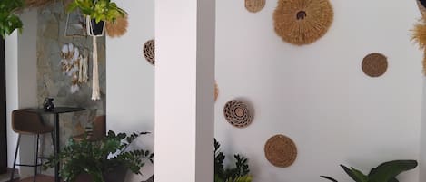 Una habitación con pared de piedra, un macramé colgante, un adorno circular tejido y una planta en maceta.