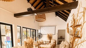 Een kamer met een hoge plafond, houten balken, een zithoek, een bank en een wandplank met decoratieve voorwerpen.