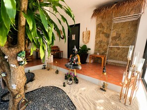 A cozy indoor space with a large tree, a stone wall, and a variety of decorative items including a statue, a small table, and a seating area. - Bohemian-style 4-bedroom villa in Bali with private pool, sauna, and ice bath; beach just a 1-minute walk away (Surat Thani)