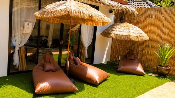 Een kamer met een glazen deur, een rieten parasol en een groen kunstgrasveld.