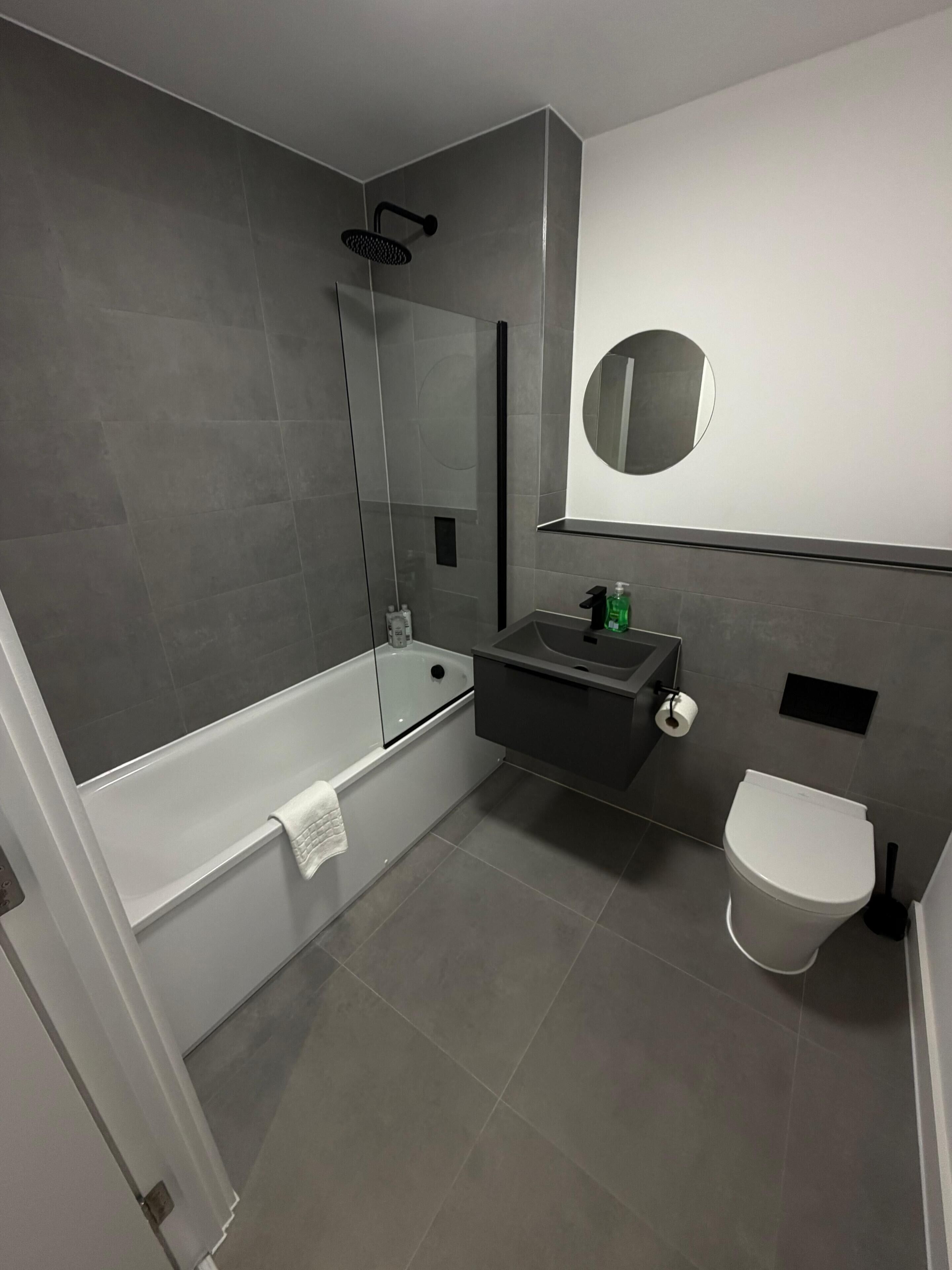 Casa de banho moderna com chuveiro envidraçado, sanita branca, lavatório com espelho e porta-toalhas.