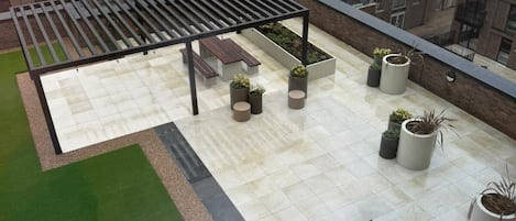 A rooftop patio with a pergola, seating, planters, and a view of surrounding buildings.