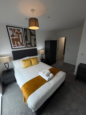 A hotel room with a large bed, two bedside tables, a wardrobe, and a door leading to another room. - Stunning 2 Bedroom Apartment-2 Bath with Balcony (Salford)