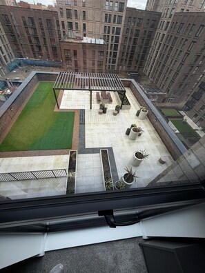 Eine Dachterrasse mit Sitzgelegenheit, Pflanzenkübeln und einem kleinen Rasen.