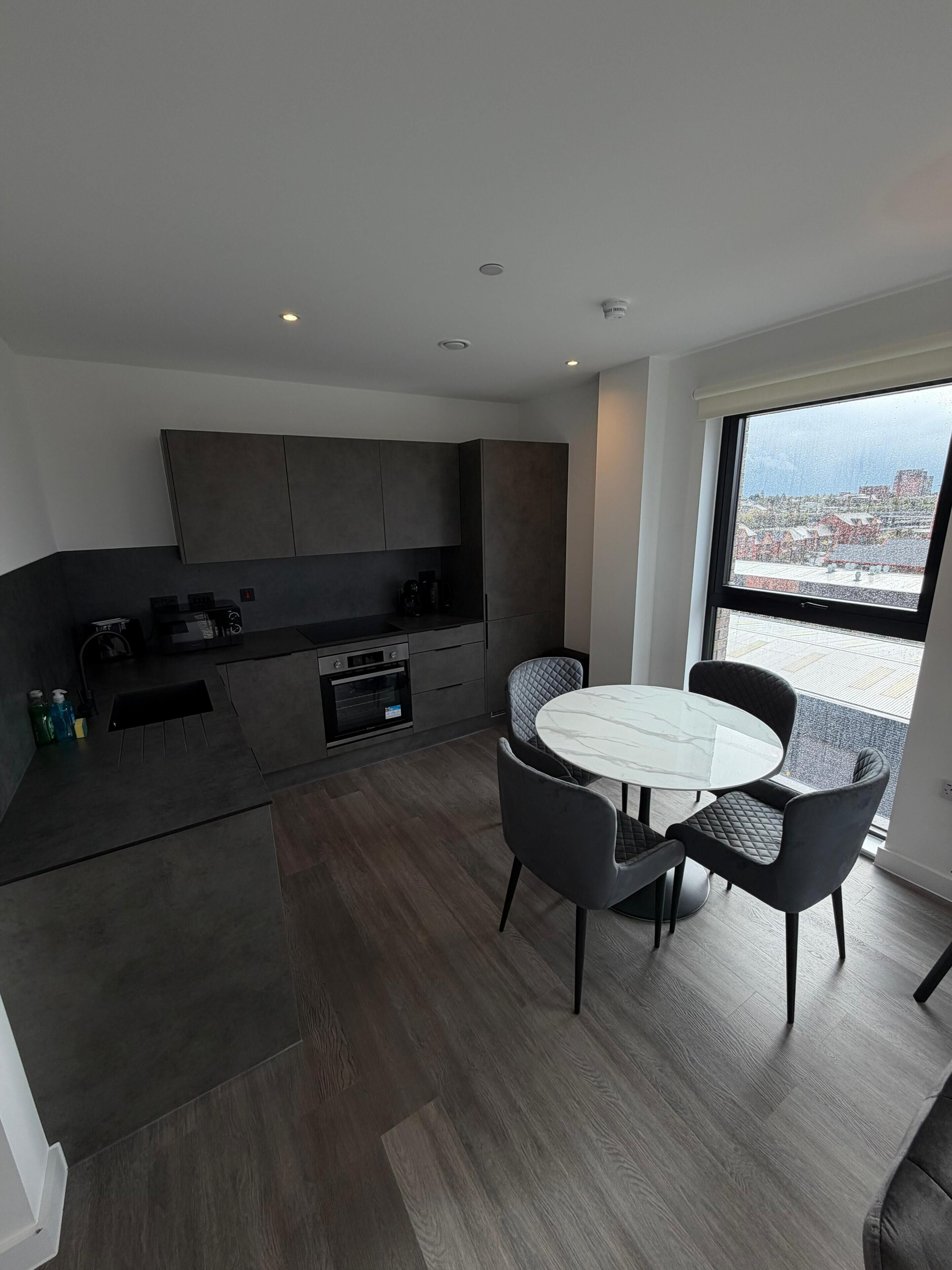 A modern kitchen with dark cabinetry, a built-in oven, and a dining area with a round table and four chairs.