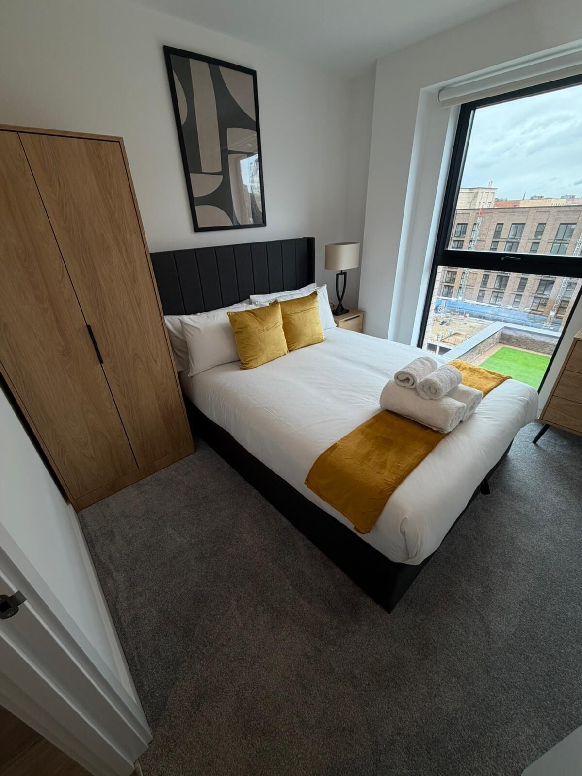 A hotel room with a bed, a wardrobe, a nightstand, a lamp, and a large window.