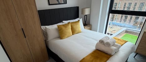 A hotel room with a bed, a wardrobe, a nightstand, a lamp, and a large window.