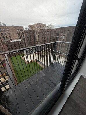 Ein Balkon mit Blick auf eine grüne Rasenfläche und Ziegelgebäude.
