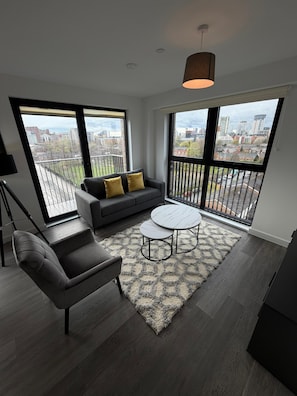 Un salon moderne comprenant un canapé, un fauteuil, une table basse et de grandes fenêtres donnant sur la ville.