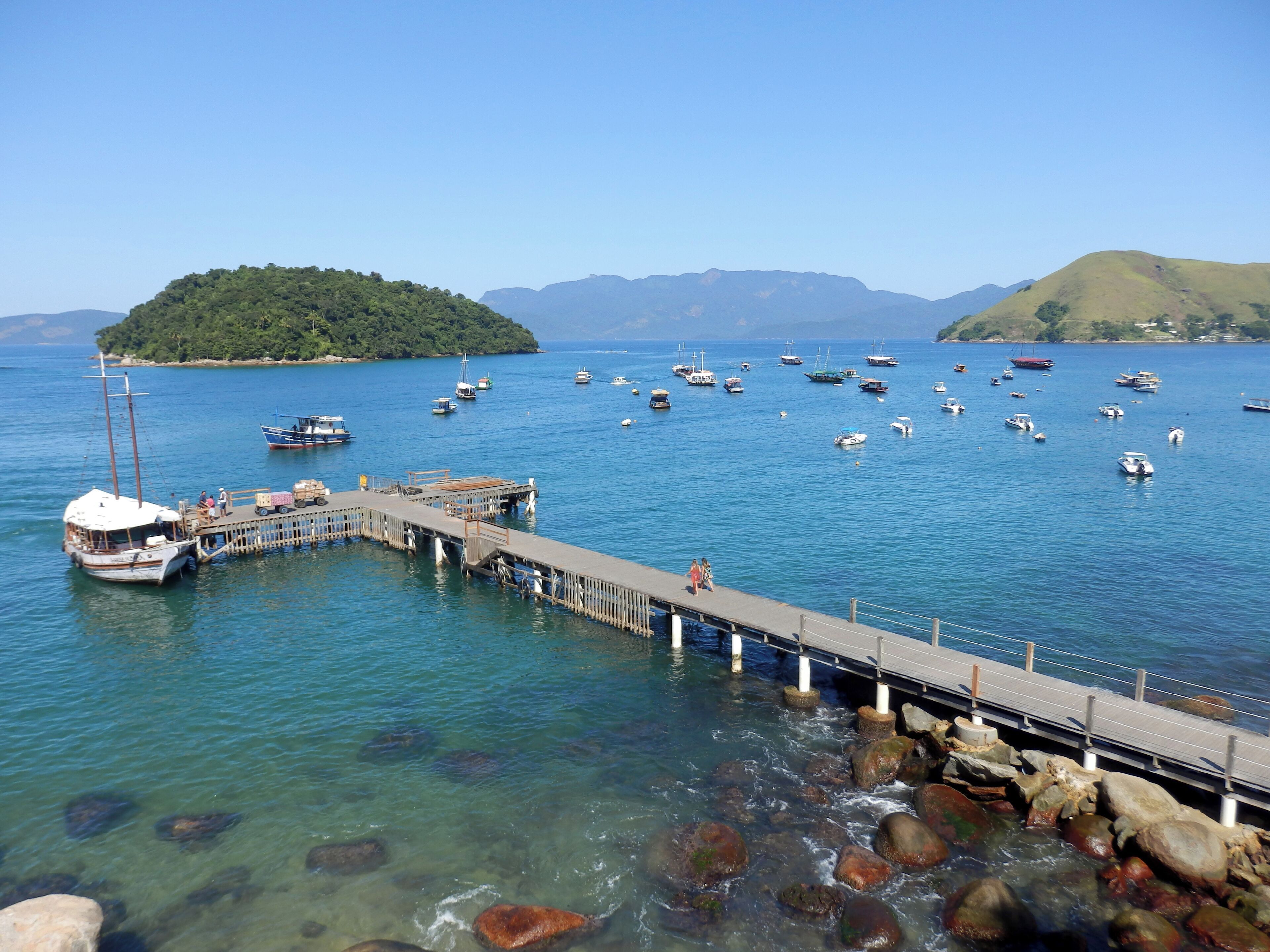 Un muelle se adentra en una masa de agua tranquila, con barcos amarrados y una pequeña isla al fondo.