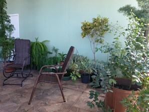 Un espace patio aménagé avec des chaises en osier, des plantes en pot et un sol carrelé en pierre.
