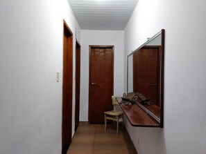 A narrow hallway with white walls, wooden doors, and a mirror on the right.