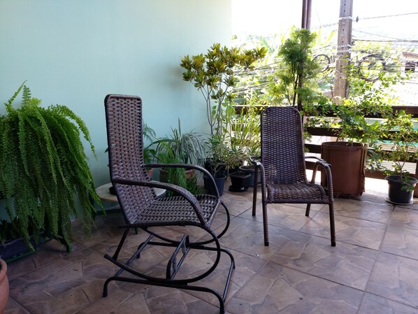 Two wicker chairs on a tiled patio with potted plants and a view of the sky.