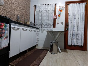 A kitchen with a sink, cabinets, a small trash bin, and a door with a curtain.
