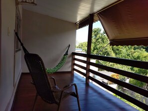A balcony with a hammock, a chair, and a view of greenery.