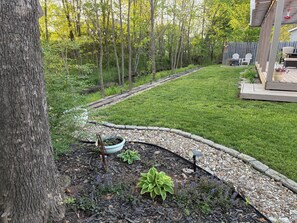 Ein Garten mit Rasen, einer Holzterrasse und einem Gartenbereich mit Pflanzen und Mulch.