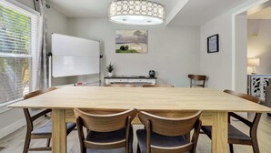 Ein Essbereich mit großem Tisch, vier Stühlen, einer Tafel, einem Gemälde und einer Pendelleuchte.