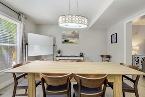 Ein Essbereich mit großem Tisch, vier Stühlen, einer Tafel, einem Gemälde und einer Pendelleuchte.