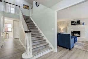 Eine Treppe mit Holzvertäfelung und weißen Geländern, die in einen Wohnbereich mit einem blauen Sofa und einem Kamin führt.
