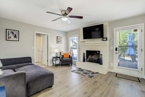 Ein Wohnzimmer mit grauem Sofa, Kamin, Fernseher darüber und Deckenventilator.