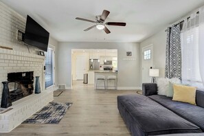 A modern living room with a fireplace, a ceiling fan, and a view into the kitchen. - Starsmore Manor! Walk to Broadmoor w/ Hot Tub (Colorado Springs)
