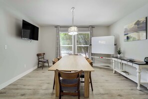 Une cuisine moderne avec une longue table en bois, des chaises, un téléviseur fixé au mur et un tableau blanc.