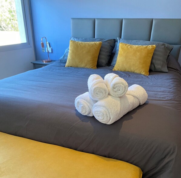 Una cama bien hecha con cabecera, almohadas y toallas enrolladas.