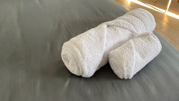 A bed with a tufted headboard, a pillow with the word 'tranqui,' and two rolled white towels.
