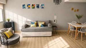 A living room with a grey sofa, a round armchair, a dining table with chairs, and artwork on the wall.