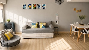 A living room with a grey sofa, a round armchair, a dining table with chairs, and artwork on the wall.