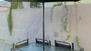 A round outdoor table with a black umbrella, surrounded by chairs, against a wall with climbing plants.